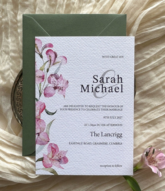 Wedding invitation card with pink lily floral design on a textured surface with green envelope