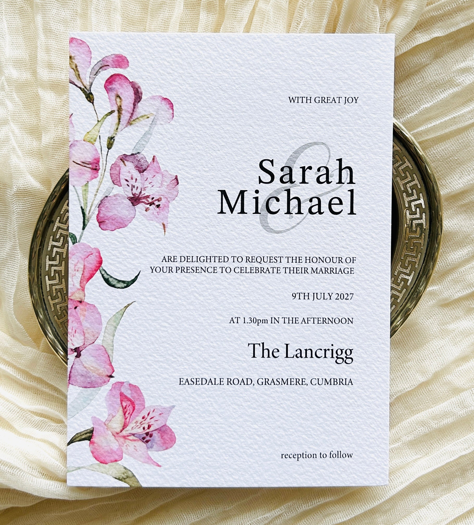 Wedding invitation card with pink lily floral design on a textured surface
