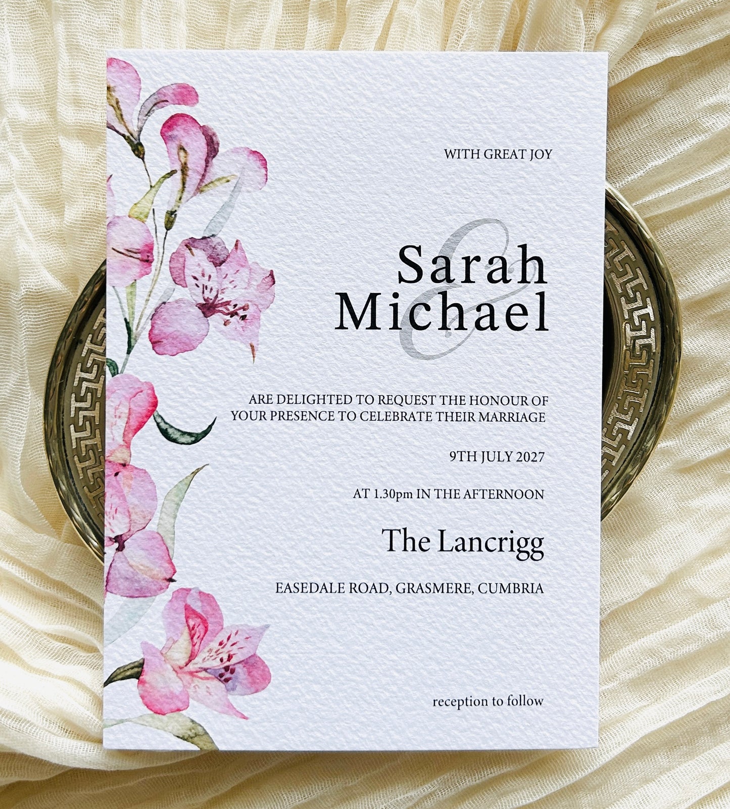 Wedding invitation card with pink lily floral design on a textured surface

