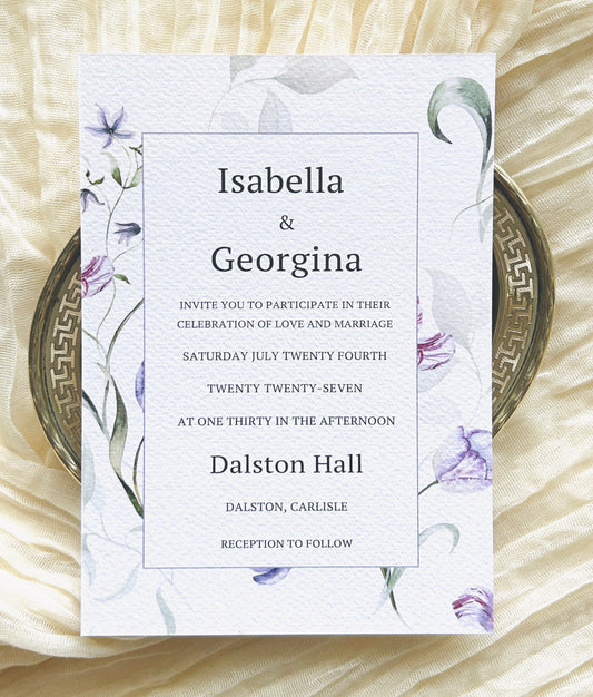 Wedding invitation card with lilac and green floral designs on a textured surface
