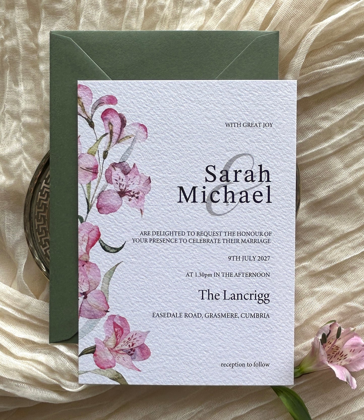Wedding invitation card with pink lily floral design on a textured surface with green envelope
