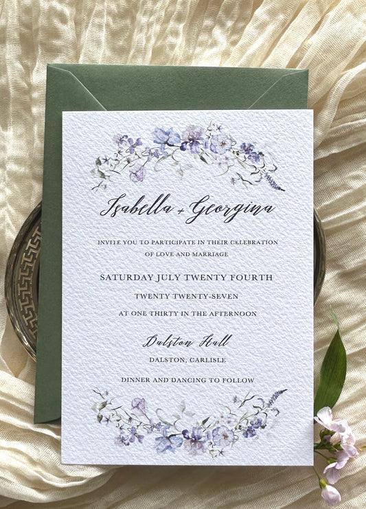 Wedding invitation card with blue, purple and pink floral design on a textured surface with green envelope
